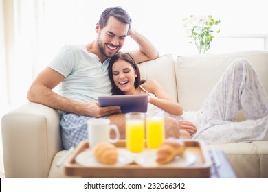 Cute couple relaxing on couch with tablet at breakfast at home in the living room - Powered by Shutterstock