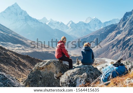 Cute Couple resting on the Everest Base Camp trekking route near Dughla 4620m. Man smiling to woman.Backpackers left Backpacks and trekking poles and enjoying valley view with Ama Dablam 6812m peak 商業照片 © 
