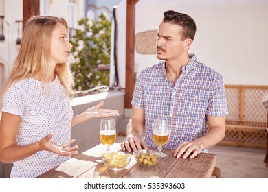 Cute couple sitting with drinks at a table in a deep discussion, while she gestures with her hands and he looking at her with concentration