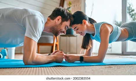 A cute couple in sportswear do an exercise plank on the mats in the living room at home. Healthy lifestyle, sports, yoga, fitness. - Powered by Shutterstock