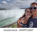 A cute couple takes a selfie in front of Niagara Falls on a sunny day in the summer