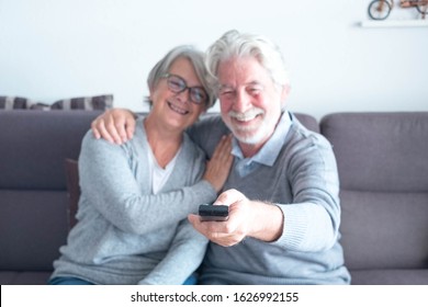 Cute Couple Of Two Caucasia Mature Seniors O The Sofa Watching  A Film Or Something In The TV - Man Holding The Remote Control