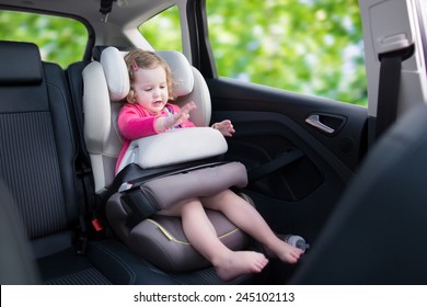 Cute Curly Laughing And Talking Toddler Girl Playing With A Toy Enjoying A Family Vacation Car Ride In A Modern Safe Vehicle Sitting In A Baby Seat With Belt Having Fun Watching Out Of The Window 