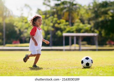 Cute curly little boy playing football. Kids play on outdoor pitch. Adorable little athlete kicking ball. Summer outdoor fun. Toddler running after ball. Sports for active child. Children exercise. - Powered by Shutterstock