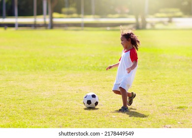 Cute Curly Little Boy Playing Football. Kids Play On Outdoor Pitch. Adorable Little Athlete Kicking Ball. Summer Outdoor Fun. Toddler Running After Ball. Sports For Active Child. Children Exercise.