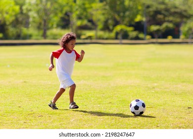 Cute Curly Little Boy Playing Football. Kids Play On Outdoor Pitch. Adorable Little Athlete Kicking Ball. Summer Outdoor Fun. Toddler Running After Ball. Sports For Active Child. Children Exercise.