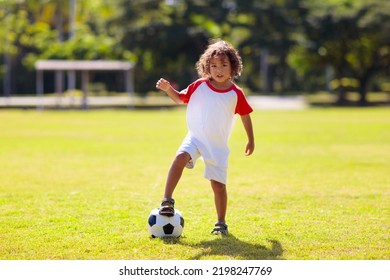 Cute Curly Little Boy Playing Football. Kids Play On Outdoor Pitch. Adorable Little Athlete Kicking Ball. Summer Outdoor Fun. Toddler Running After Ball. Sports For Active Child. Children Exercise.