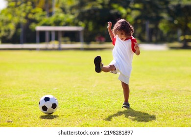 Cute Curly Little Boy Playing Football. Kids Play On Outdoor Pitch. Adorable Little Athlete Kicking Ball. Summer Outdoor Fun. Toddler Running After Ball. Sports For Active Child. Children Exercise.