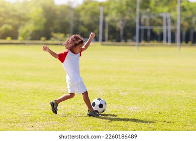 Cute curly little boy playing football. Kids play on outdoor pitch. Adorable little athlete kicking ball. Summer outdoor fun. Toddler running after ball. Sports for active child. Children exercise. - Powered by Shutterstock
