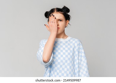 Cute Dark-haired Teen Girl Making Facepalm, Child Covers Half Of Face With Palm, Seriously Looks With One Eye At Camera, Stands In Trendy T Shirt Over Light Grey Background