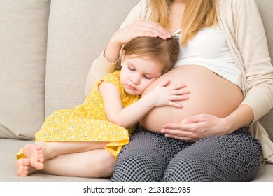 Cute Daughter With Closed Eyes Sitting On Sofa At Home, Cuddling Pregnant Mother Big Belly With Hands And Waiting Future Brother Or Sister. Emotional Lovely Moment. Baby Expectation. Pregnancy Time. 