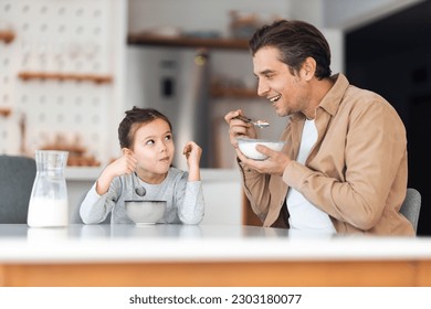 A cute daughter eating a bowl of cereal and milk with her smiling father in the sunny dining room. - Powered by Shutterstock