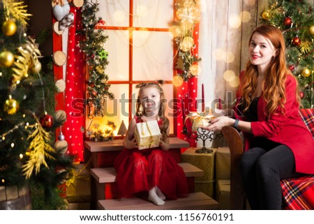 Cute daughter and mother holding presents in a studio with a warm christmas decor. Cosy gold and red decor