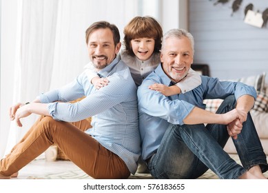 Cute delighted child hugging his father and grandfather
