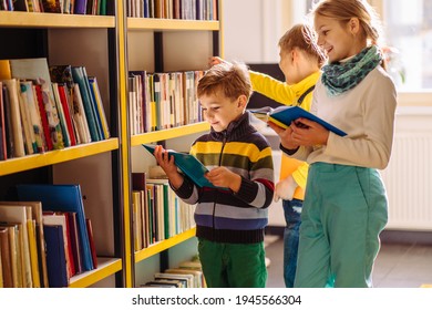 Cute different age pupils, two boys and girl looking for books in library at the elementary school. Three children standing near bookshelves and reading together at school's library. - Powered by Shutterstock