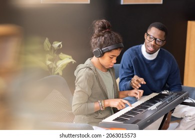 Cute diligent schoolgirl pushing keys of piano keyboard while teacher helping her during home lesson - Powered by Shutterstock