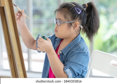 Cute Disability Kid Artist Enjoys Creative Painting Craft. Asian Special Girl Preschoolers Pay Attend Drawing Art In Classroom. Occupational Therapy Learning Disablilities Education Concept.