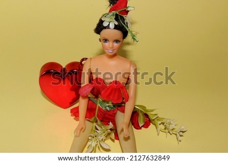  cute doll dressed in a dress of red and white flowers with a white flower in her hair and a red heart behind her on a yellow background creative concept dressing in nature