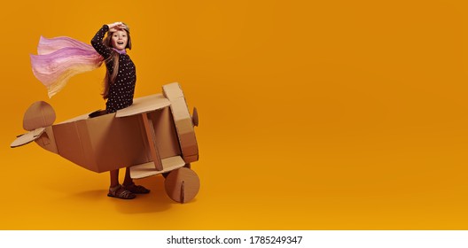 Cute dreamer girl playing with a cardboard airplane. Childhood. Fantasy, imagination. Studio portrait on a yellow background. - Shutterstock ID 1785249347
