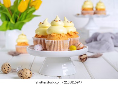 Cute Easter chick cupcakes. Vanilla cupcakes with buttercream on a white stand with fresh flowers on a white wooden background. Copy space