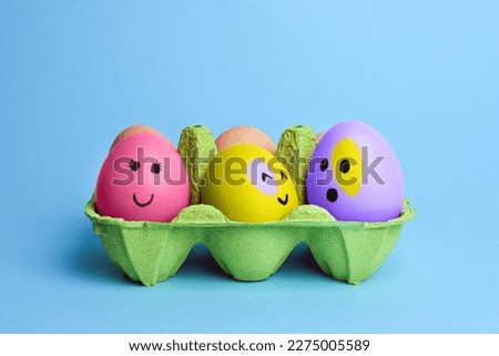 Cute easter eggs with funny faces in green box isolated on light blue background. Happy easter concept. Painted Easter eggs.