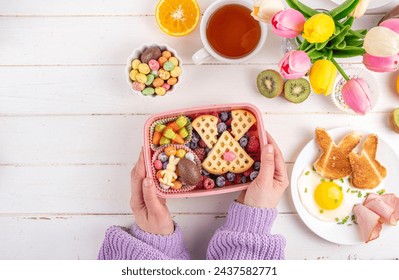 Cute Easter style lunchbox. Creative kids school lunch box with Easter symbols and sweets - bunny rabbit belgian waffle sandwiches, berry fruit, candy carrots, chocolate eggs - Powered by Shutterstock