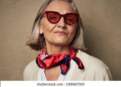 Cute Elderly Woman In Sunglasses With A Scarf Around Her Neck On An Isolated Background