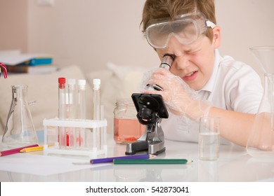 Cute elementary schoolboy looking into microscope at his desk at home. Young scientist making experiments in his home laboratory. Indoors. Child and science. Education concept. - Powered by Shutterstock