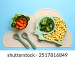 Cute elephant-themed baby feeding set with healthy food on blue background.