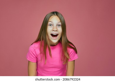 Cute emotional little girl child surprised looking at camera feeling astonished, wondered, amazed on pink background