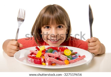 cute European female child smiling happy eating candy with spoon fork and knife in sugar abuse , unhealthy sweet nutrition concept , children candy addiction and kids  dental care