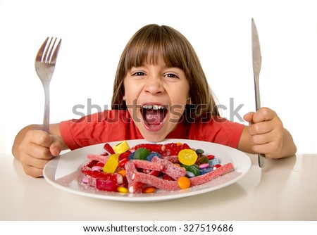 cute European female child smiling happy eating candy like crazy with fork and knife in sugar abuse , unhealthy sweet nutrition concept , children candy addiction and kids  dental care