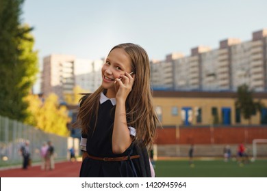 Cute european schoolgirl smiling at the camera, talking on smartphone. Apprentice secondary school intercommunicate by mobile device at schoolyard. Technology, mobile telephony and people concept - Shutterstock ID 1420945964