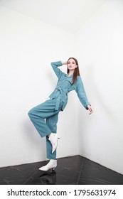 Cute European teenage girl posing for a catalog shooting in studio, as if falling and showing it with facial extensions and pose, looking at camera. Wearing navy blue summer suit and white boots