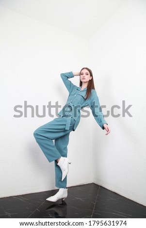 Cute European teenage girl posing for a catalog shooting in studio, as if falling and showing it with facial extensions and pose, looking at camera. Wearing navy blue summer suit and white boots