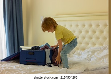 a cute fair-haired child boy folds clothes in an open suitcase on the bed. travel preparation, childhood.