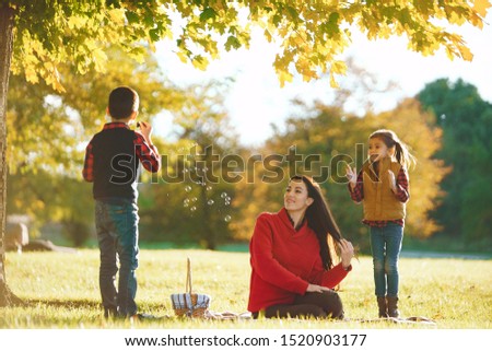 Cute family in a autumn park. Happy mother with little kids. Family playing on yellow leaves. Golden autumn.
