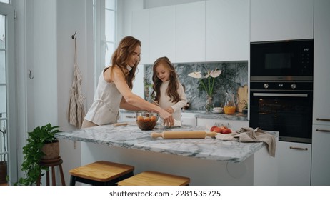 Cute family cooking at kitchen together. Young woman and child girl preparing dough on table. Mother daughter sifting flour in modern interior house. Adorable kid helping parent at light white home - Powered by Shutterstock