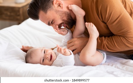 Cute Father Cuddling Bonding With Little Baby Daughter Spending Time Together Lying On Bed At Home. Loving Daddy Laughing Playing With Toddler. Fatherhood, Dad's Love, Child Care And Parenting Joy