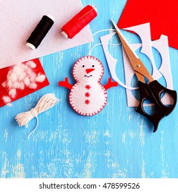 Cute Felt Christmas Snowman Ornament, Scissors, Thread, Needle, Cord, Felt Sheets And Scraps On Wooden Background. Supplies For Making Handmade Snowman. Christmas Kids Crafts Background Idea. Top View