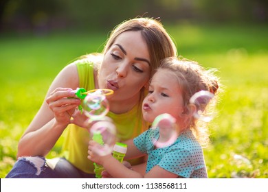 Cute female child blows soup foam and make bubbles with her mother in nature