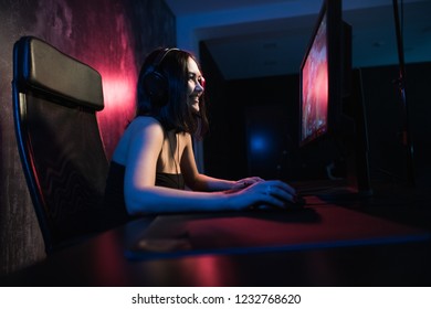 A cute female gamer girl sits in a cozy room behind a computer and plays games. Woman live streaming computer video games to her fans and wiggle hand to them. Streamer and gamer concept.