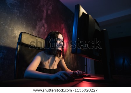 A cute female gamer girl sits in a cozy room behind a computer and plays games. Woman live streaming computer video games to her fans. Streamer and gamer concept