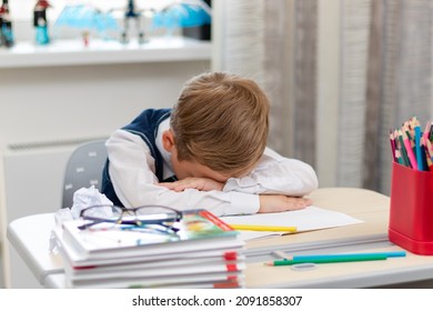 A cute first grader boy in a school uniform at home during a pandemic fell asleep doing homework at a desk with books and pencils. Selective focus. Close-up. Portrait