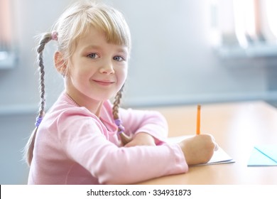 Cute Five Years Old  Blonde Girl Sitting At Classroom And Writing