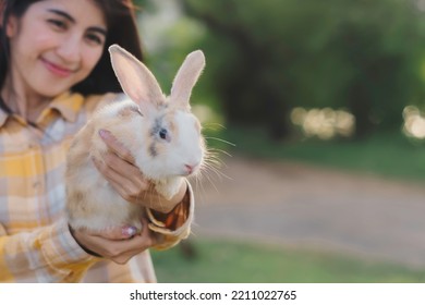 Cute And Fluffy Rabbit In Woman's Hand With Backlit Light Of Sunset In Evening, Blur Smile Of Happiness's Asian Girl And Green Backyard And Space.