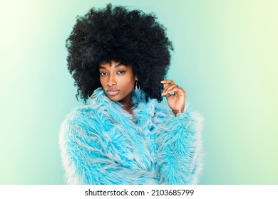 Cute Funky Young Black Woman Wearing A Stylish Fluffy Cool Blue Winter Top Posing Over A Matching Blue Studio Background