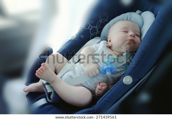Cute funny baby boy is sleeping in car ?hild safety\
seat, image with toning, blur background and effect of soft shining\
sun