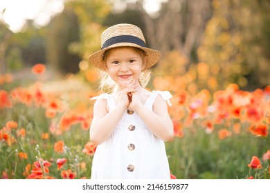 Cute Funny Baby Girl 2-3 Year Old Wear Straw Hat And White Summer Dress Over Flower Meadow Background. Kid Laughing Outdoors Over Nature. Looking At Camera. Childhood. 