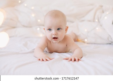 Cute funny baby lying on bed. Baby  girl learning to crawl and playing in white sunny bedroom.  Little child doing tummy time. 